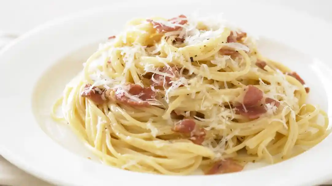 A plate of creamy spaghetti carbonara topped with crispy bacon and grated Parmesan cheese, garnished with black pepper.