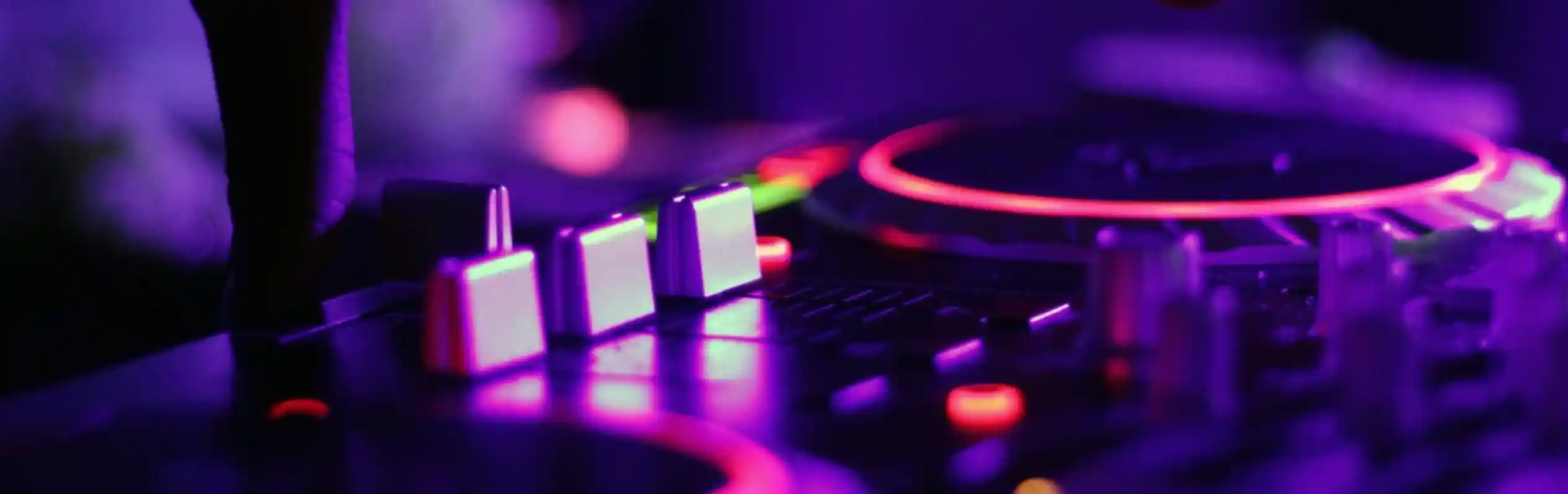 A close-up of a hand adjusting a DJ mixer with glowing knobs and buttons in purple lighting.