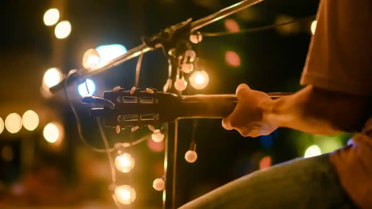 A close-up of a musician's hand holding a guitar, with soft glowing lights in the background, creating an intimate atmosphere.