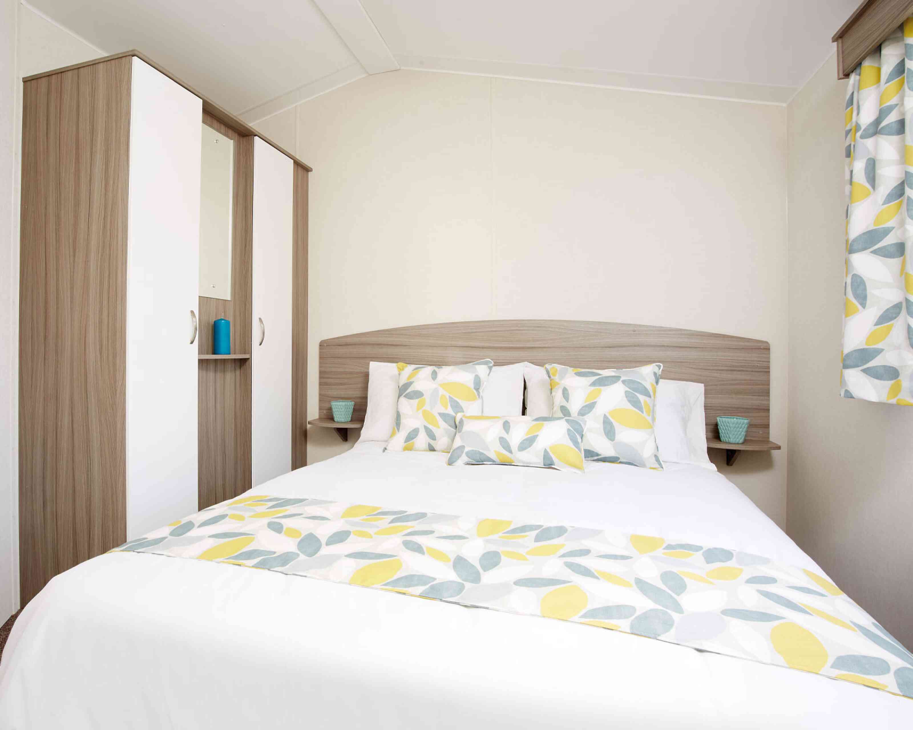 A bright bedroom with a bed dressed in yellow and white bedding, complemented by a wooden dresser nearby.