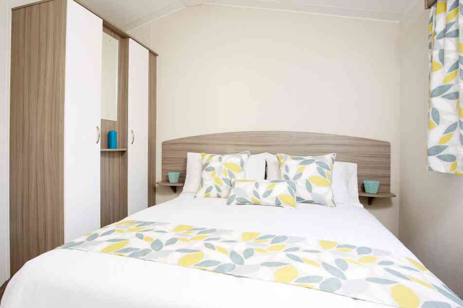 A bright bedroom with a bed dressed in yellow and white bedding, complemented by a wooden dresser nearby.