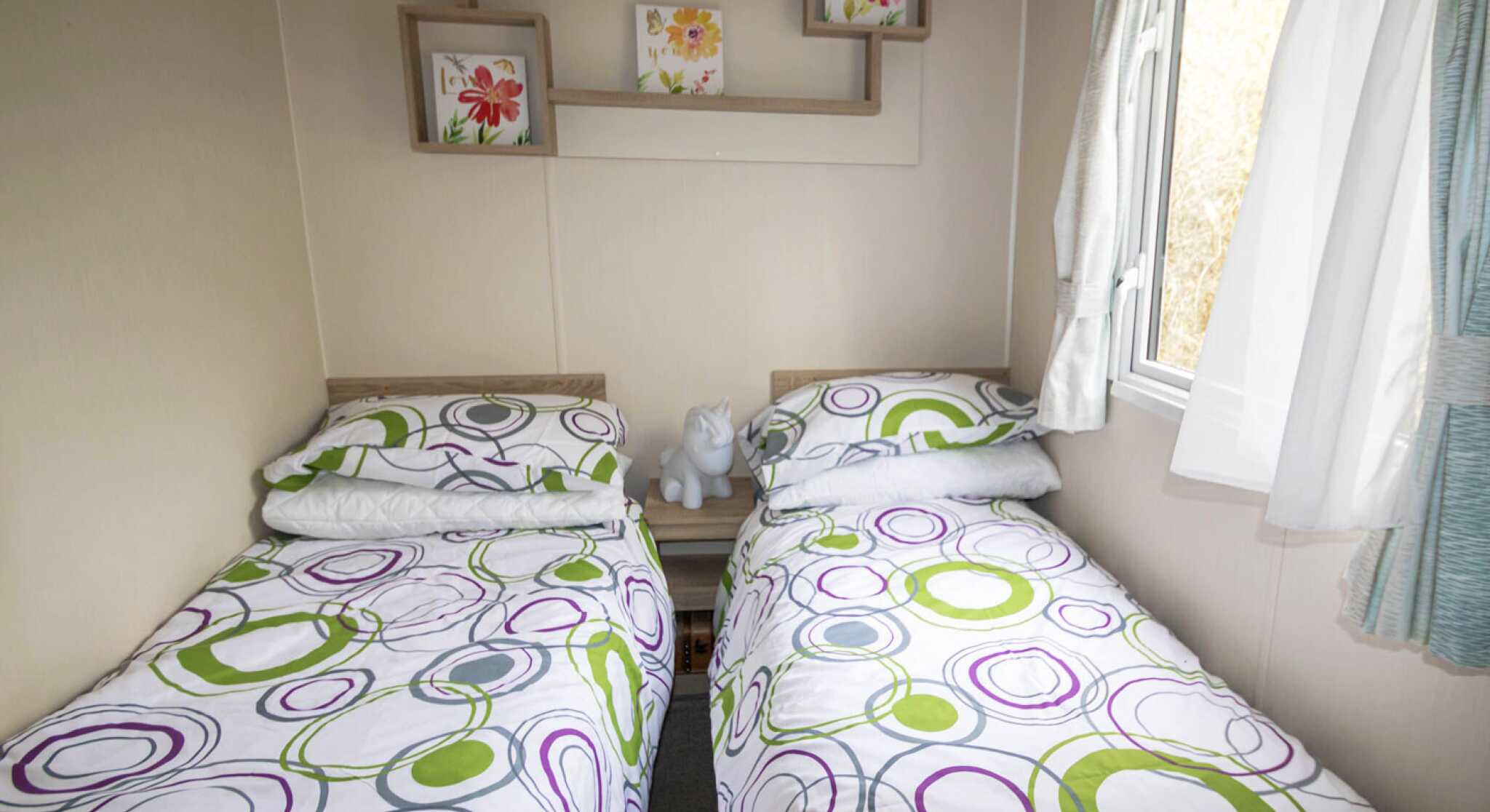 A second bedroom featuring two twin beds, neatly made with simple bedding and a window allowing natural light