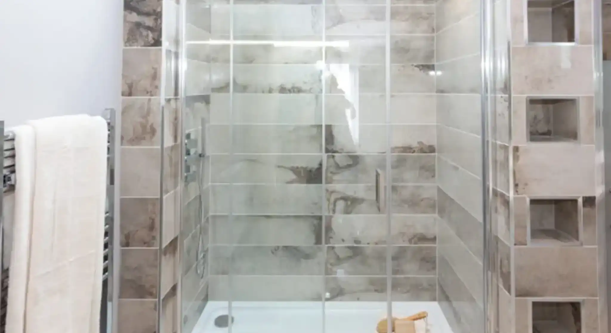A modern shower enclosure with glass doors, tiled walls, a white shower base, and a towel rack with white towels.