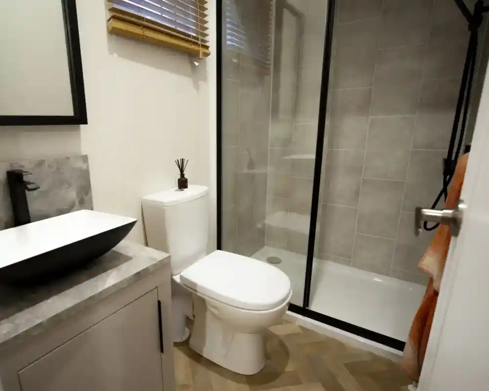 Modern bathroom with a black and white vessel sink, a white toilet, and a glass-enclosed shower with grey tiled walls.