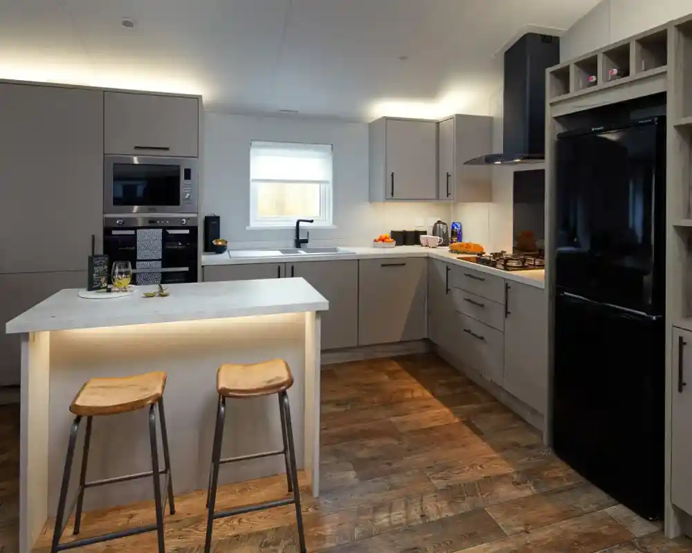 Modern kitchen with grey cabinets, stainless steel appliances, a black refrigerator, and a central island with two stools.