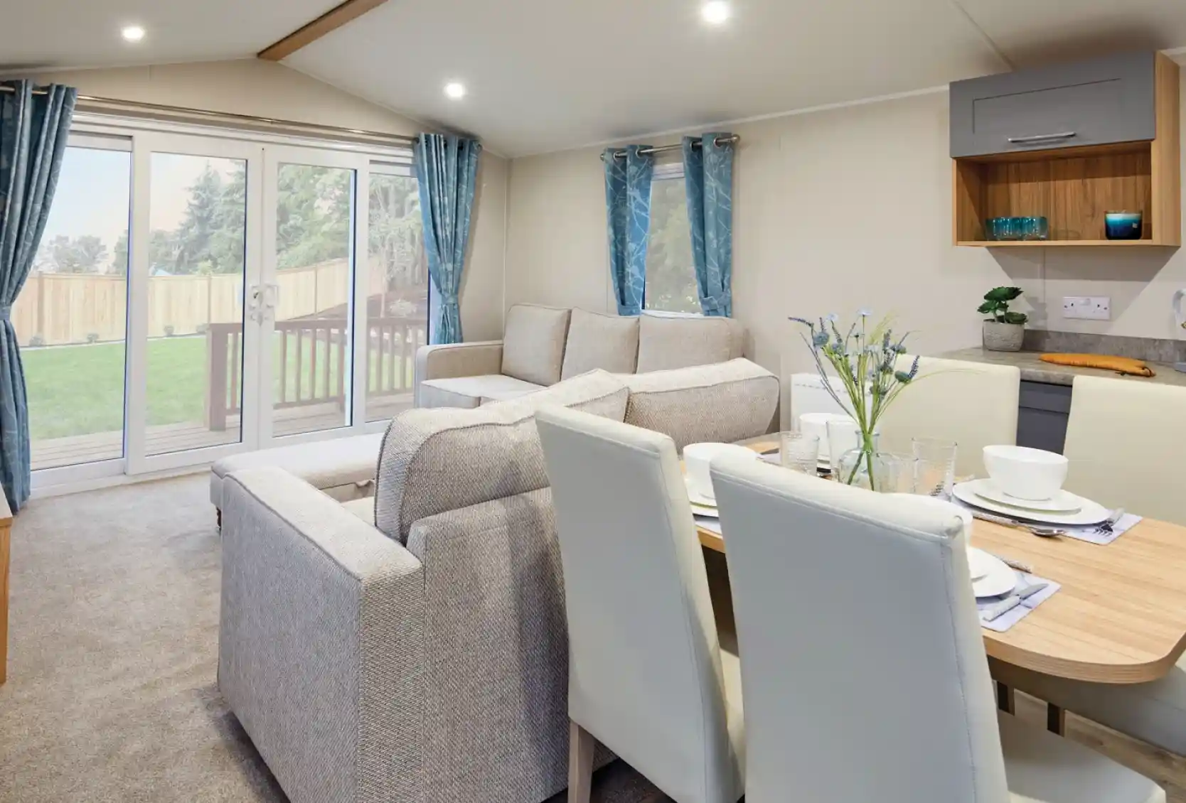 Modern living room and dining area with a two beige sofas, a dining table with cream dining chairs, and sliding glass doors leading outside.