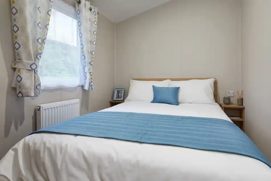 Bright master bedroom in a holiday caravan with white linens, blue accents, light wood furniture, and soft neutral décor for a calm, inviting feel.
