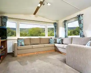 Corner sectional sofa in a living room with large bay windows overlooking a green, hilly landscape.