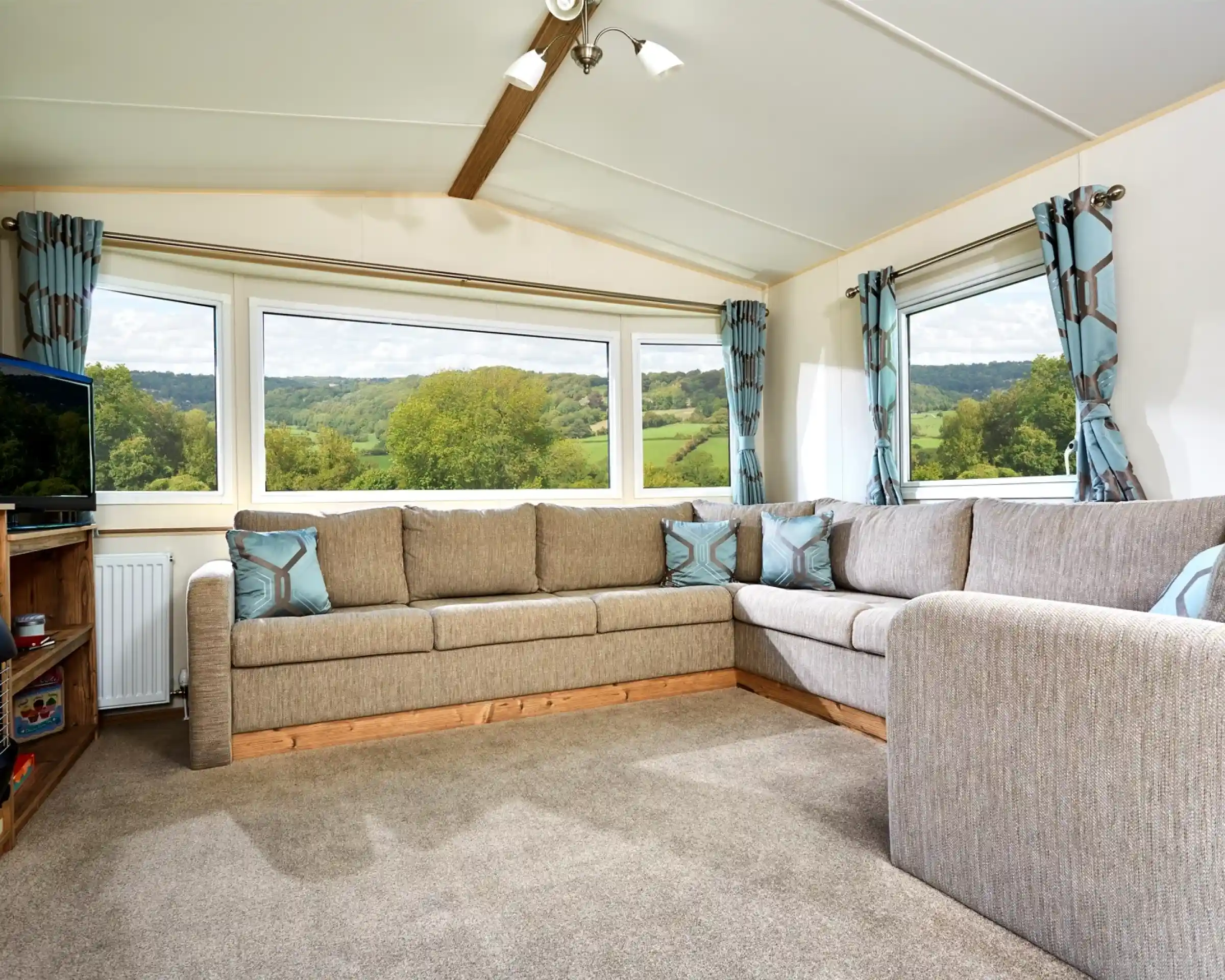 Corner sectional sofa in a living room with large bay windows overlooking a green, hilly landscape.
