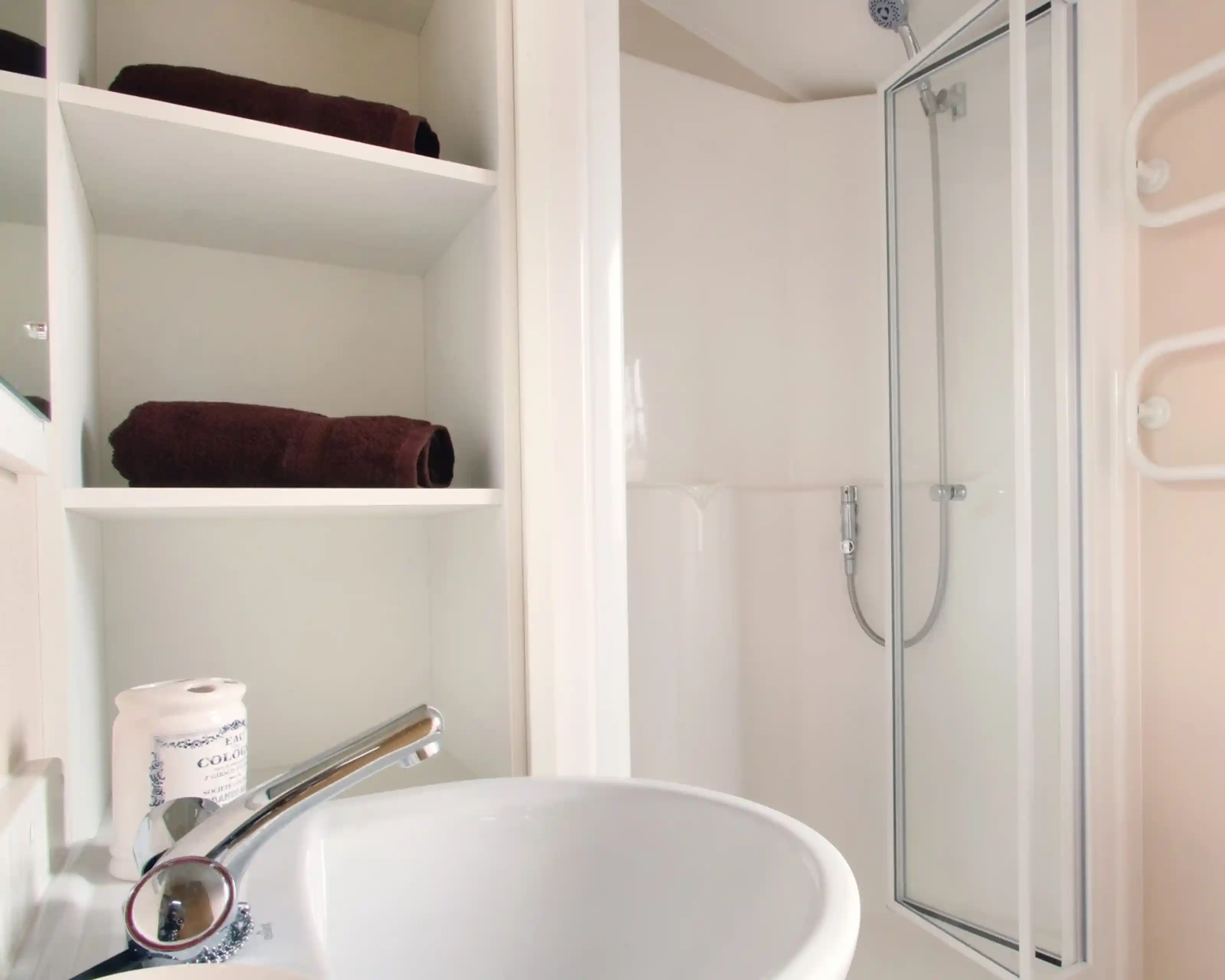 A shower room with enclosed shower, wash basin and shelving.