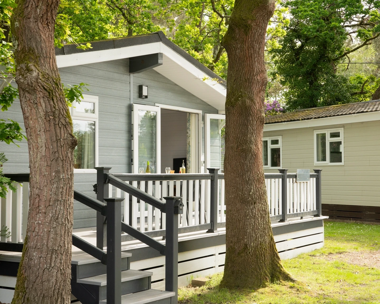 Close-up view of a stylish lodge with outdoor decking and patio furniture, surrounded by greenery at Forest Edge.