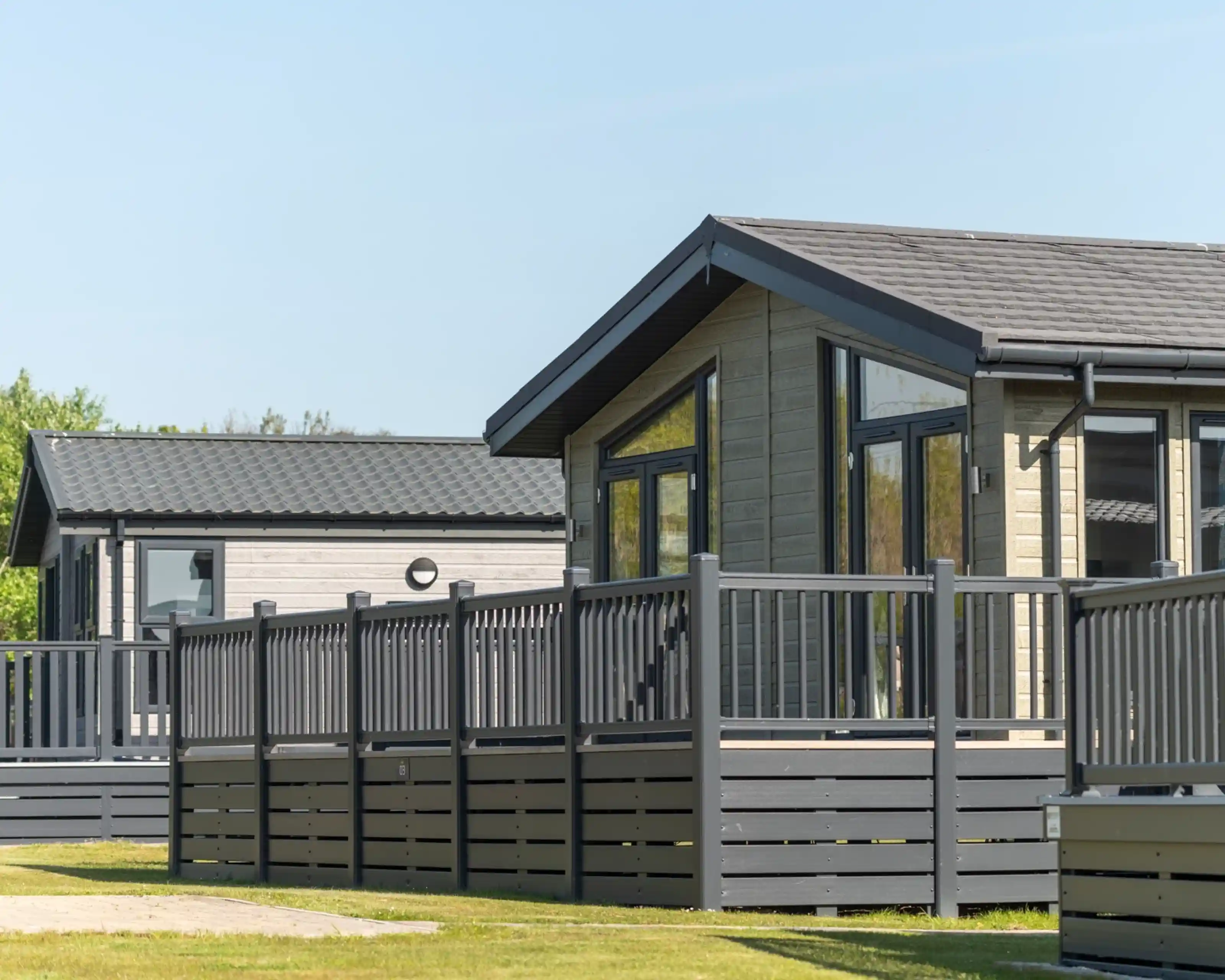 Modern cabins with wooden decks in a landscaped area under a clear blue sky. Green grass surrounds the cabins, creating a serene outdoor atmosphere.