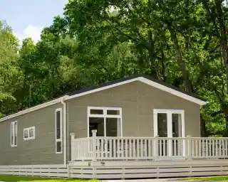 A modern house with a light green exterior and a spacious white deck is surrounded by lush trees and greenery.