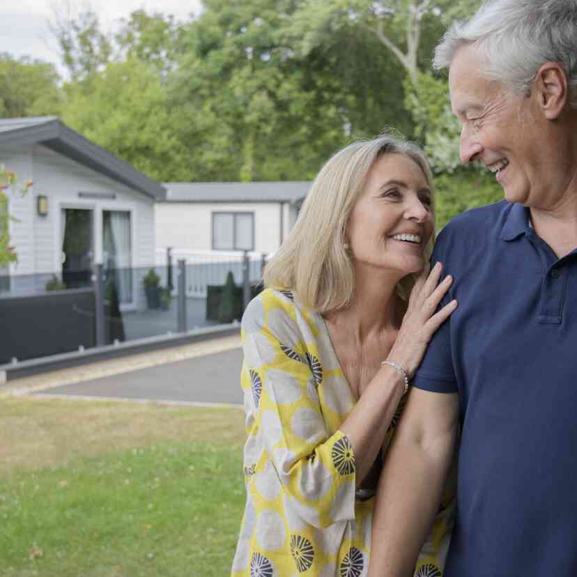 A senior couple poses in front of their mobile home, showcasing a warm and cheerful moment together.