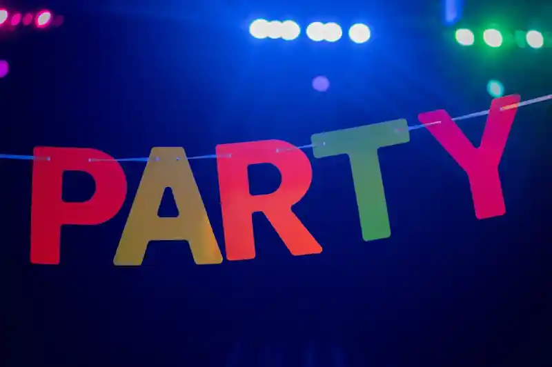 Colorful letters spelling "PARTY" are strung across a dark background, illuminated by vibrant blue and purple lights.