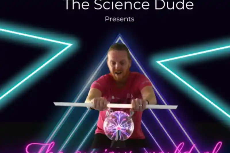 A man in a pink shirt is demonstrating a science experiment involving a clear sphere, surrounded by neon triangular shapes and bright lighting. The text above reads "The Science Dude Presents" and below, "The curious world of."