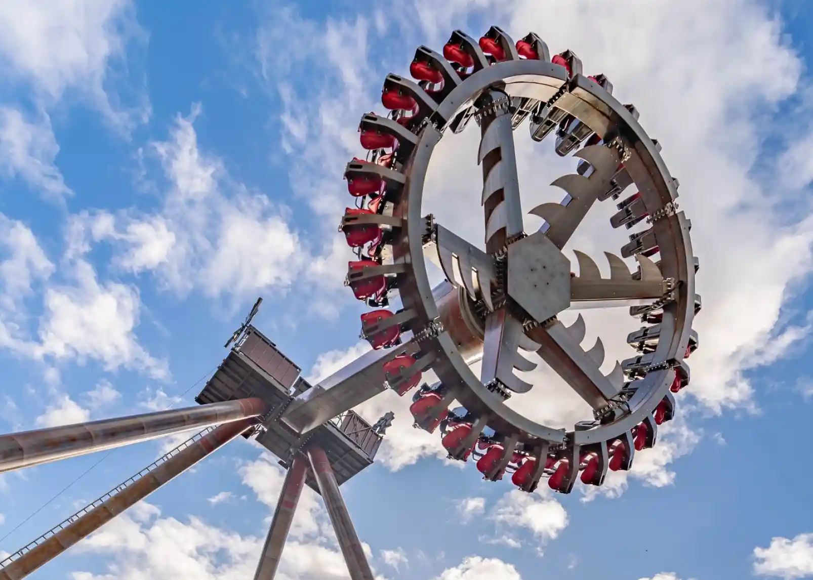 A large amusement park ride featuring a rotating circular structure with seats attached, set against a blue sky with fluffy white clouds.